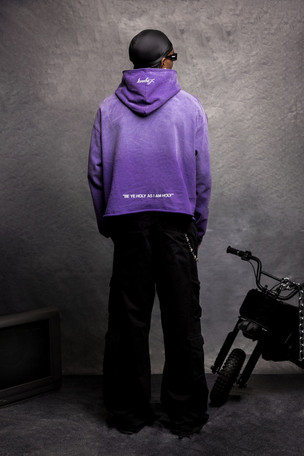 Black JUST BE GOD hoodie by Legaxy Studios displayed on a hanger with front design visible.